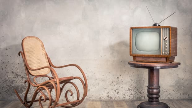 大约20世纪50年代的复古老式电视接收器放在木桌上，在纹理混凝土墙背景前的老摇椅上。